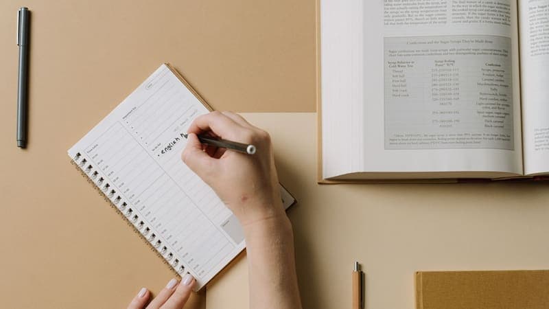 Hands writing a to-do list in a daily planner beside an open textbook