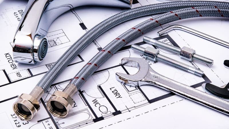 Wrench, braided supply hoses and a faucet lying on a building floor plan