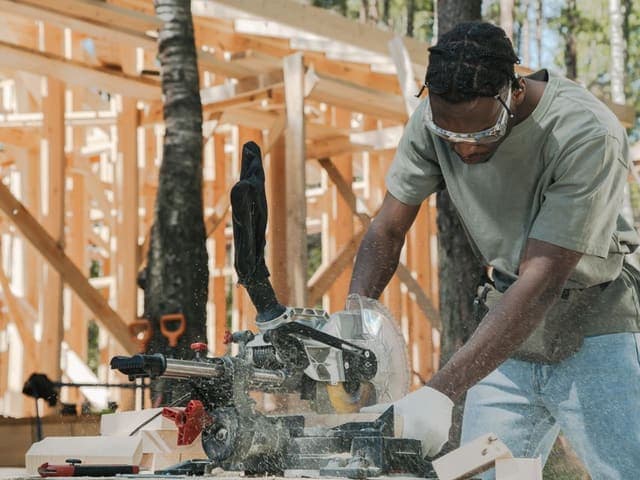Carpenter cutting lumber with a miter saw beside new wood framing