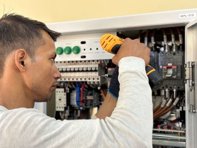 Electrician using a drill on a circuit breaker panel