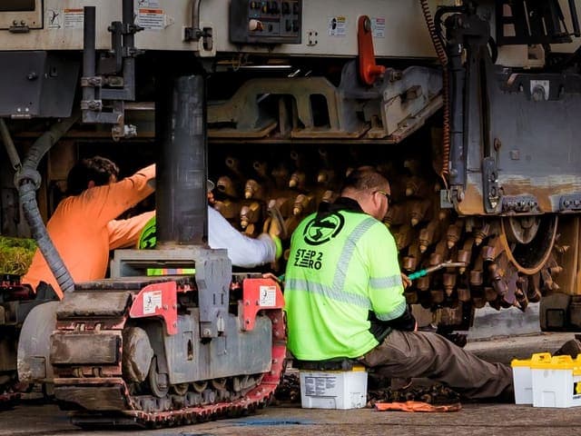 Mechanics servicing the undercarriage of a tracked construction machine