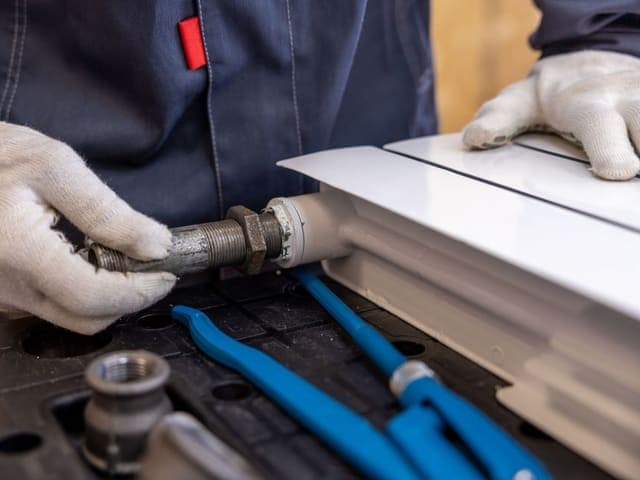 Plumber in work gloves fitting a threaded pipe to a radiator