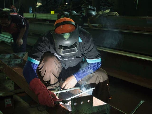 Welder in a helmet welding a steel beam in a workshop
